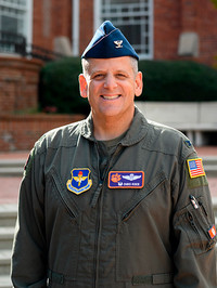 Portrait of a military officer in a flight suit, wearing a cap and various insignia.