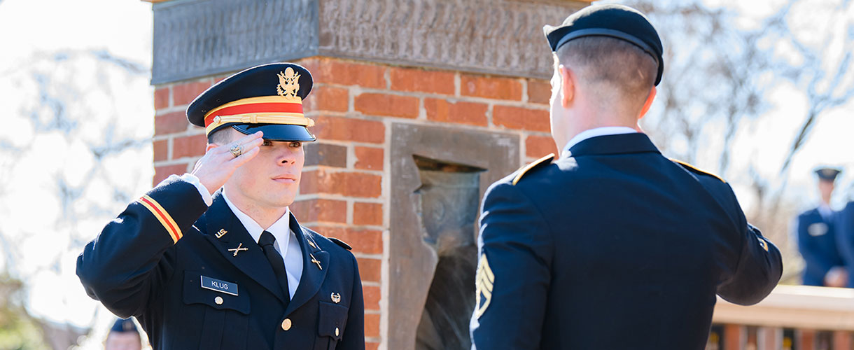 Two men in Army dress uniforms facing each other and saluting one another.