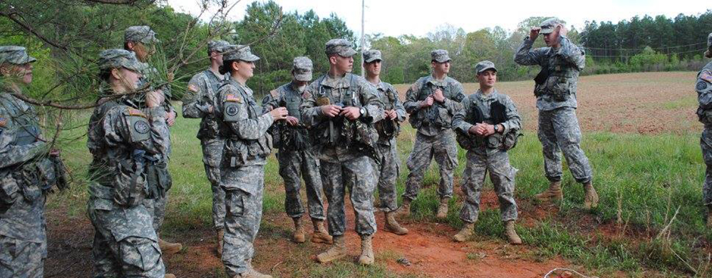 Cadets in camouflage in classroom taking notes.