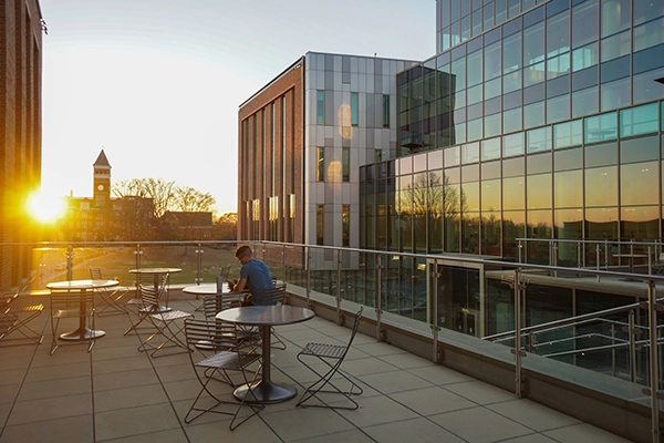 A scenic outdoor terrace with modern furniture, featuring a person sitting alone as the sun sets behind a building.