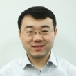 A professional headshot of a man with glasses, wearing a light-colored shirt and smiling.