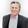 Professional headshot of a middle-aged man in a suit, smiling confidently.