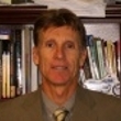 Professional headshot of a man in a suit with a bookshelf in the background.