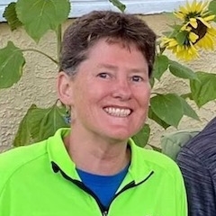Smiling individual wearing a bright green jacket, standing in front of sunflowers.