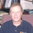 A portrait of a smiling man sitting in an office environment.