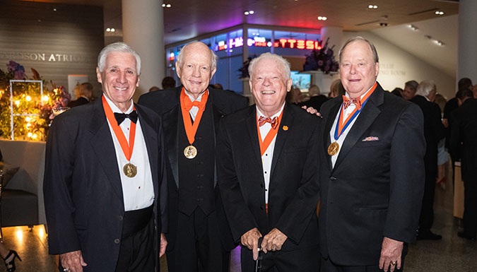 Four distinguished men wearing tuxedos and medals at a formal event, all smiling and posing together.