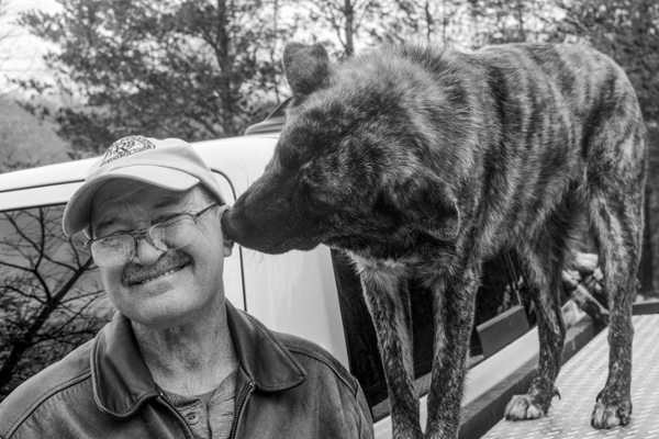 A man smiling with a dog playfully kissing his cheek, both enjoying a moment together outdoors.
