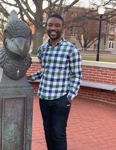 A person smiling while standing next to a large eagle statue in a campus setting.