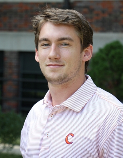 A young man with short brown hair wearing a striped polo shirt featuring a 'C' logo.