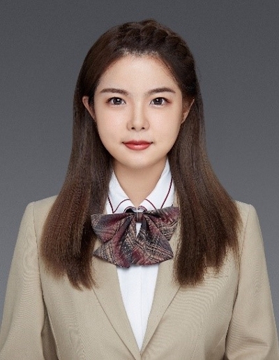 Professional portrait of a young woman wearing a beige blazer and bow tie, with straight hair styled down.