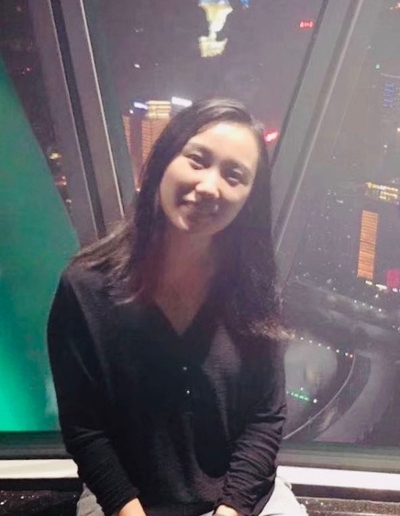 A smiling woman sits in front of a city skyline at night, illuminated by colorful lights.