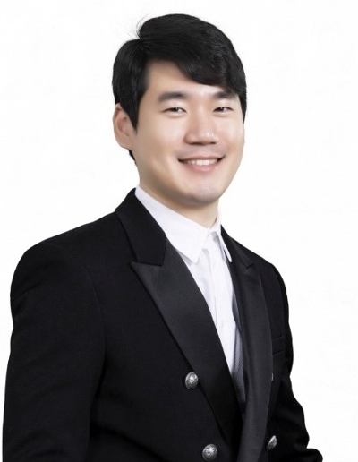 Formal portrait of a man in a tuxedo, smiling confidently against a plain background.