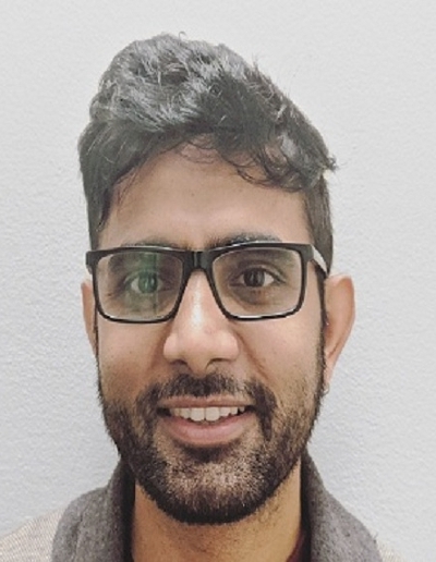 Headshot of a man with glasses and a beard, smiling against a plain background.