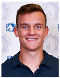 Headshot of a smiling young man with short hair, wearing a navy polo shirt, set against a background featuring a horse logo.