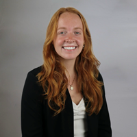 Female with long red hair wearing white shirt and black jacket.