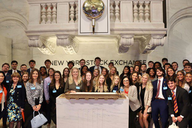 Group photo of students visiting the New York Stock Exchange, posing in front of the trading floor.