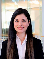 Professional headshot of a woman in a black blazer and white shirt, smiling against a modern, bright background.