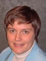 Professional headshot of a woman with short hair, wearing a light blue jacket and white turtleneck.