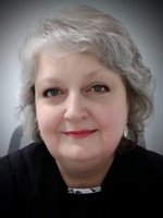 A smiling woman with shoulder-length gray hair and subtle makeup, wearing a black top.