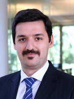 Professional headshot of a man in a suit with a mustache and a patterned tie.