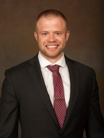 Professional headshot of a smiling man in a black suit and red tie.