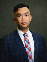 Professional headshot of a young man wearing a plaid suit and colorful tie.