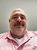 A smiling man with a bald head and a beard, wearing a pink polo shirt.