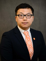 A professional portrait of a man wearing glasses, a dark suit, and a patterned orange tie.