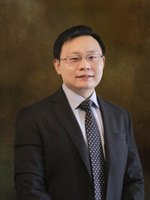 Professional portrait of a man in a suit with a patterned tie against a textured background.