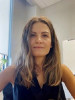 Professional portrait of a woman with long, wavy hair, sitting at a desk in an office setting.