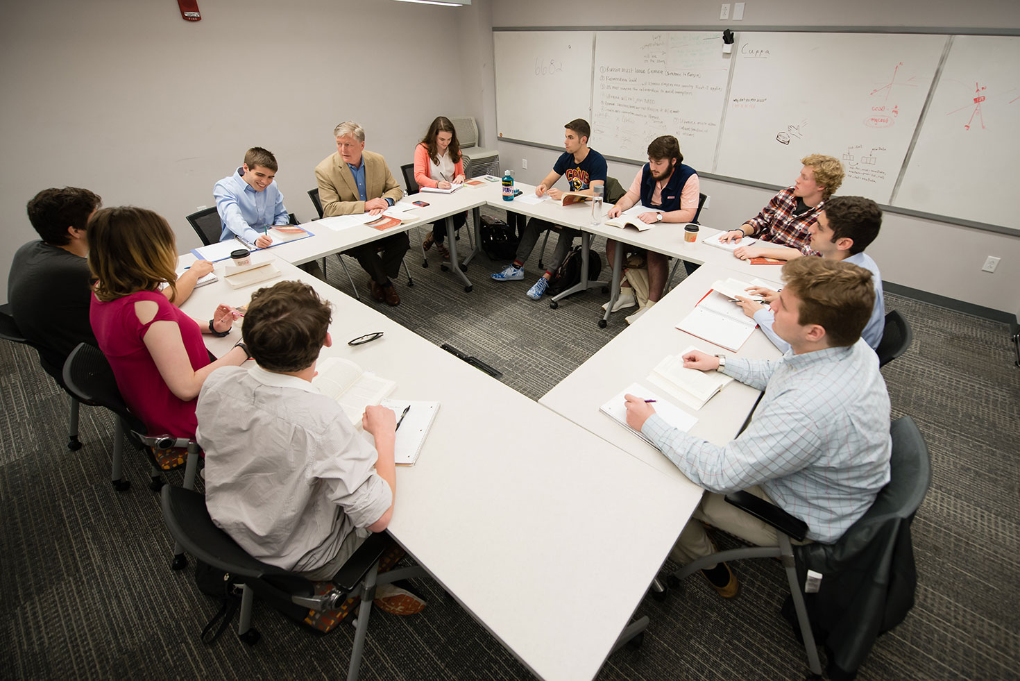 Many students sitting at tables in a square pattern in classroom.