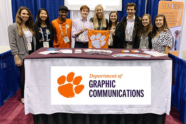Graphics Communication students standing at booth behind table and holding tiger rag.