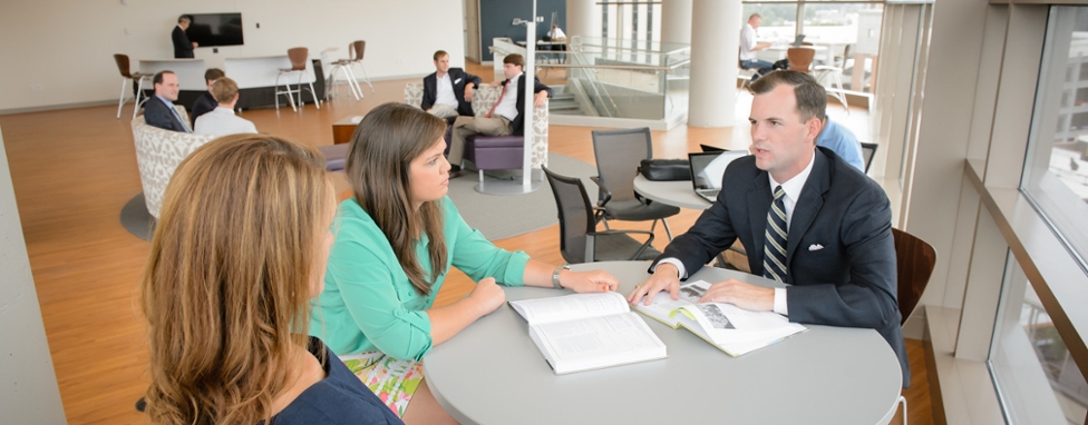 Two female and one male student sitting at table working on laptops.