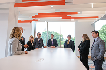 Faculty standing in conference room with Tillman Hall in the background of the window behind them.