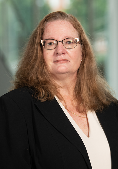 Professional portrait of a woman with long brown hair wearing glasses and a black blazer.
