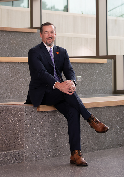 Portrait of a man in a suit sitting on a bench, smiling confidently in a well-lit modern space.