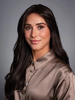 Studio headshot of a woman with long dark hair wearing a satin blouse, facing slightly to the side against a gray background.