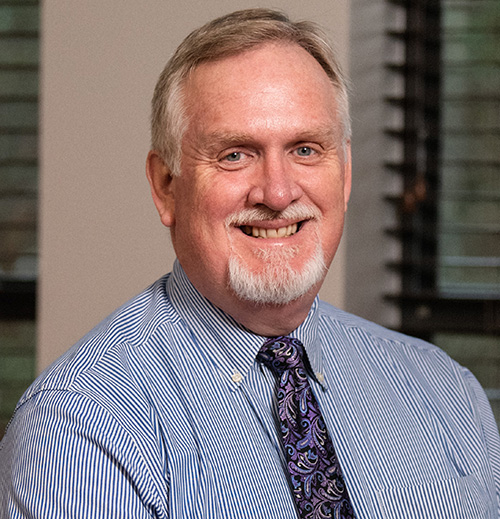 Man with short gray hair wearing a blue striped button-up shirt.