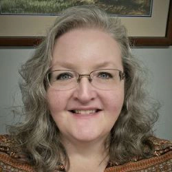 Portrait of a woman with curly hair and glasses, smiling at the camera.