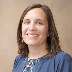 Portrait of a smiling woman with shoulder-length brown hair wearing a blue shirt with decorative patterns.
