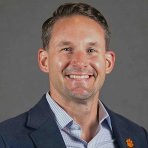 Professional headshot of a smiling man in a blazer, showcasing a friendly demeanor.