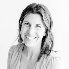 A black and white portrait of a smiling woman with wavy hair, wearing a light-colored top.