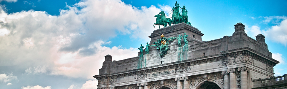 Gray building with green horse statues on top and clear blue sky in background.