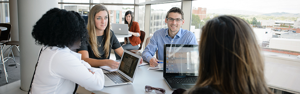 Three females and one male sitting around table with laptops.