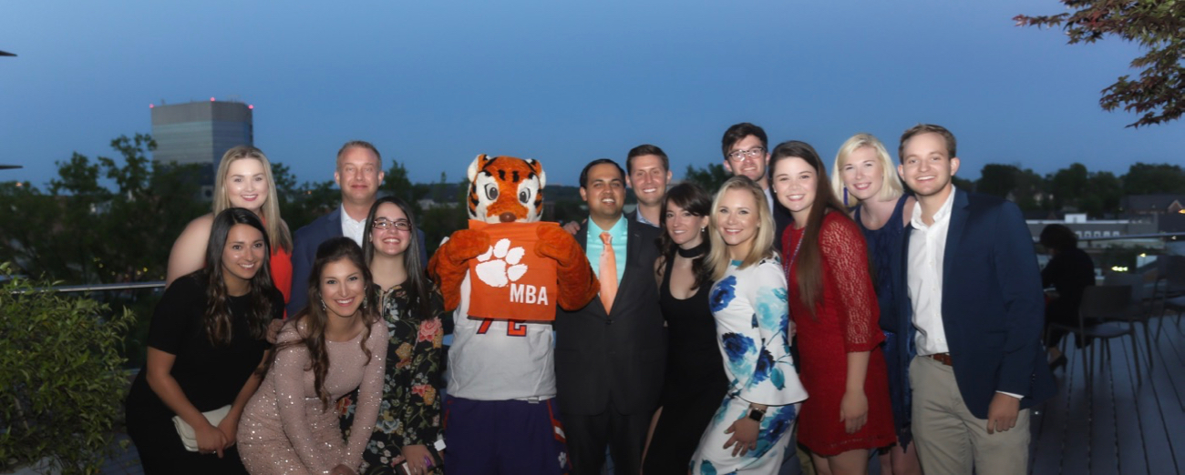 Group of male and female students posing with Tiger mascot and Tiger Rag that says MBA with tiger paw.
