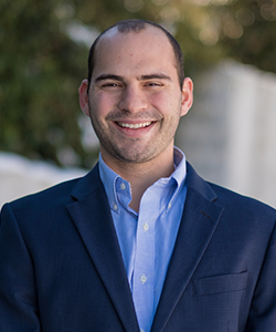 Head shot of man in blue suit with short dark hair and brown eyes.