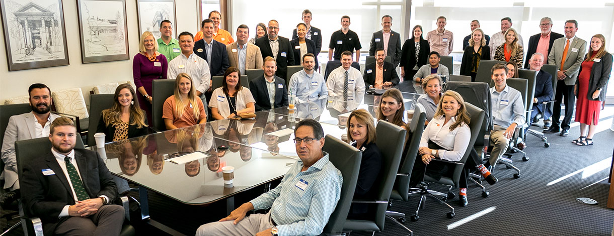 Large group of people standing and sitting around a large conference table.