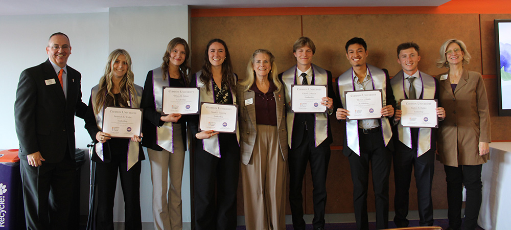 Group photo of award recipients holding certificates, accompanied by university faculty and staff at a recognition event.