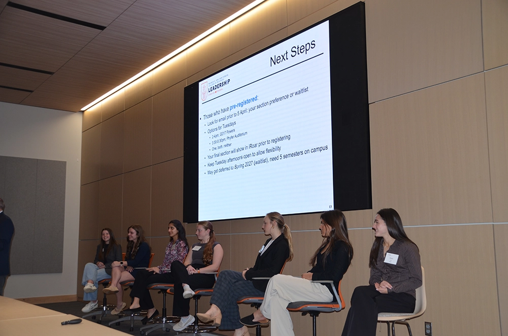 Panel of students seated on stage beneath a large screen displaying a “Next Steps” presentation slide.