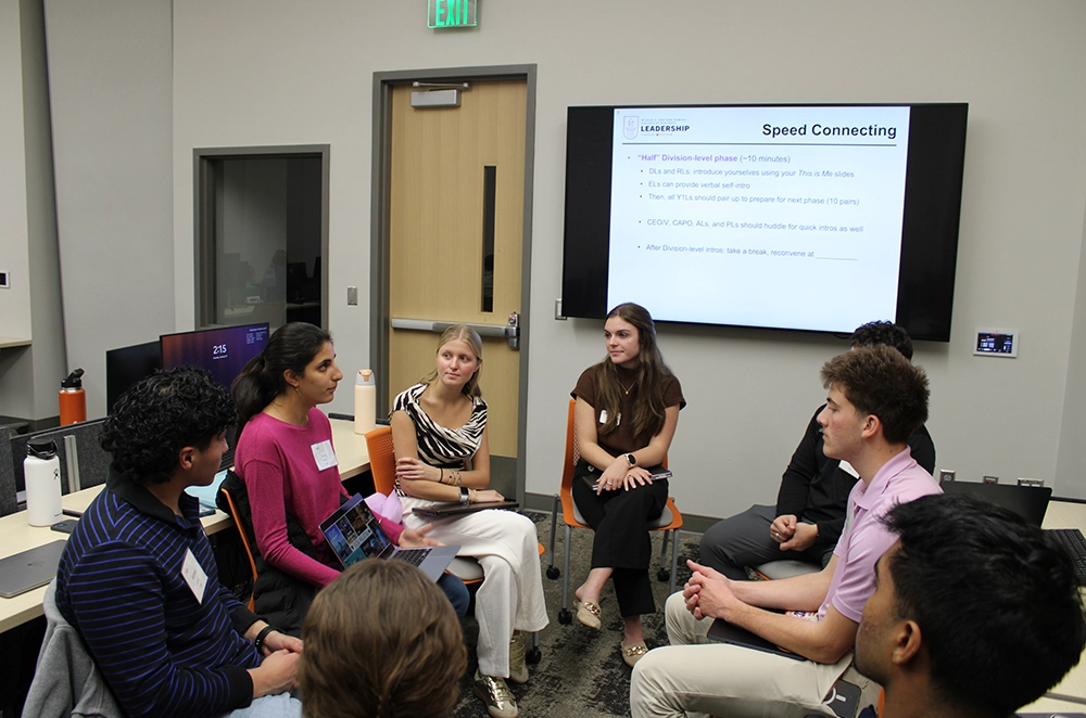 Small group seated in a classroom for a speed networking discussion, with a “Speed Connecting” slide displayed on a screen.